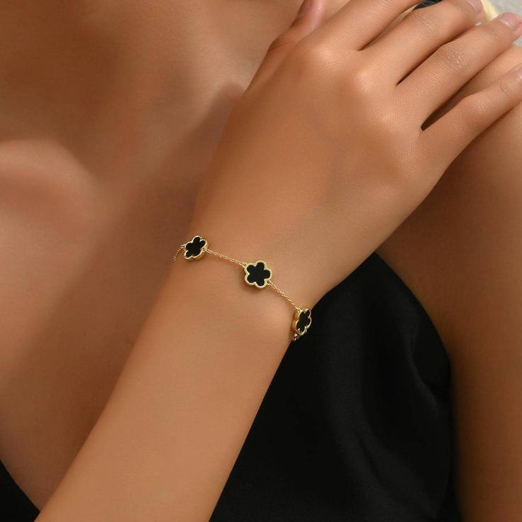 Gold bracelet with black clover charms on a person's wrist against a neutral background