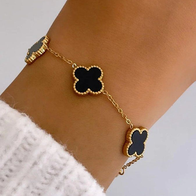 Gold bracelet with black clover charms on a person's wrist against a neutral background
